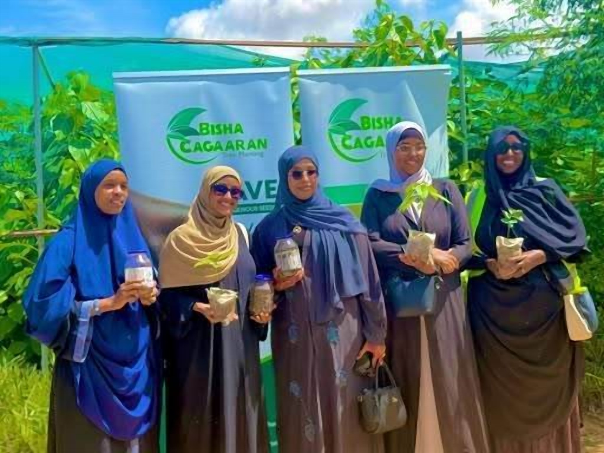 Women holding small tree seedlings at a tree-planting event.