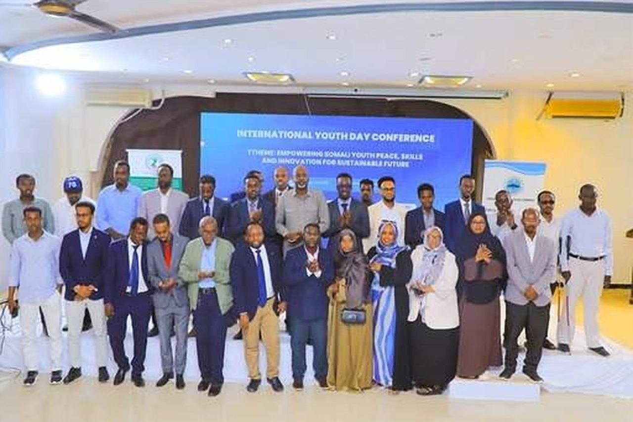 A large group of men and women posing together in front of the International Youth Day Conference screen.