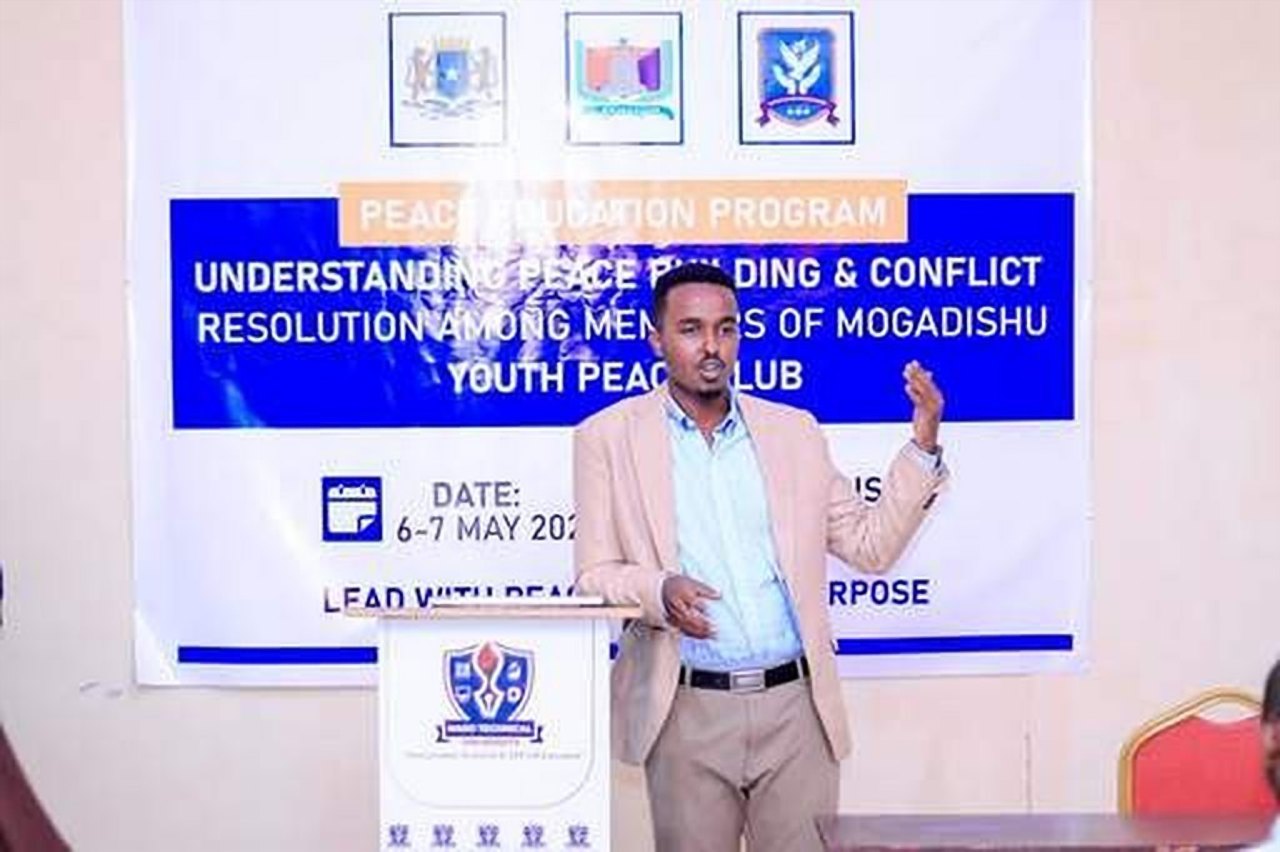A trainer standing at a lectern in front of a Peace Education Program banner.