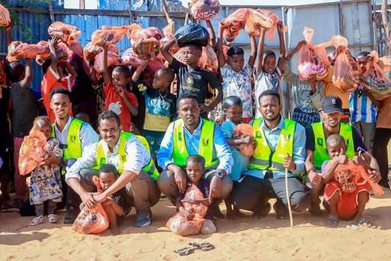Volunteers in yellow safety vests crouching with smiling children who are holding bags.
